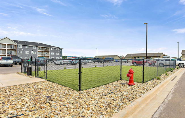 A red fire hydrant sits on a gravel area next to a black fence.