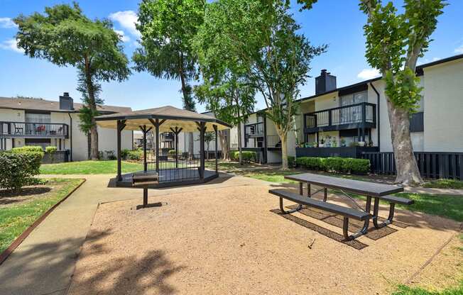 a picnic area with benches and trees in front of apartment buildings