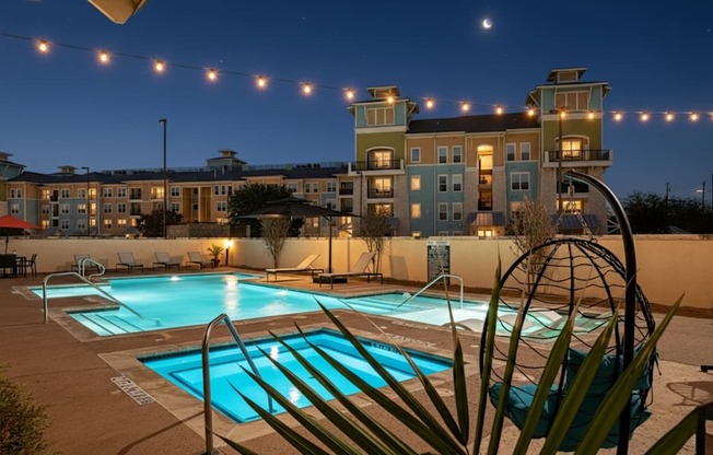 A pool area with a building in the background and lights strung above.