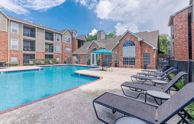 A pool surrounded by lounge chairs and a brick building.