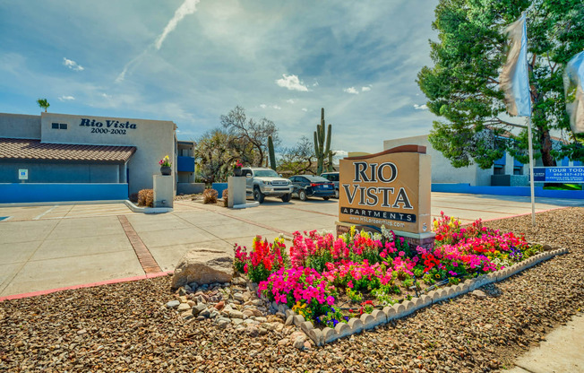a sign for the rio vista entrance with flowers in front of a building