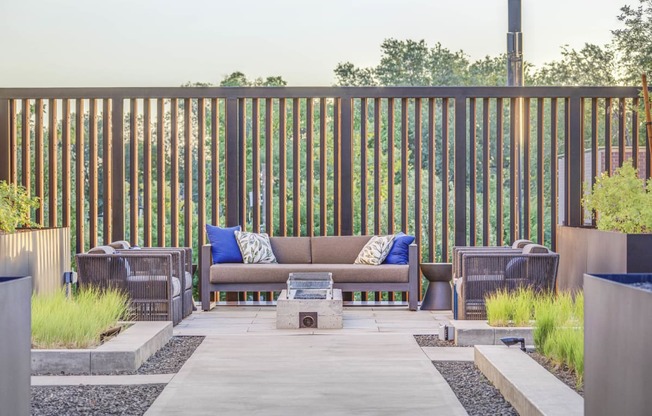 a patio with a couch and chairs with a fire pit in the middle