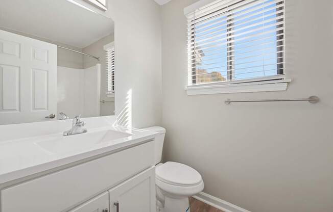 A white bathroom with a toilet, sink, and window.