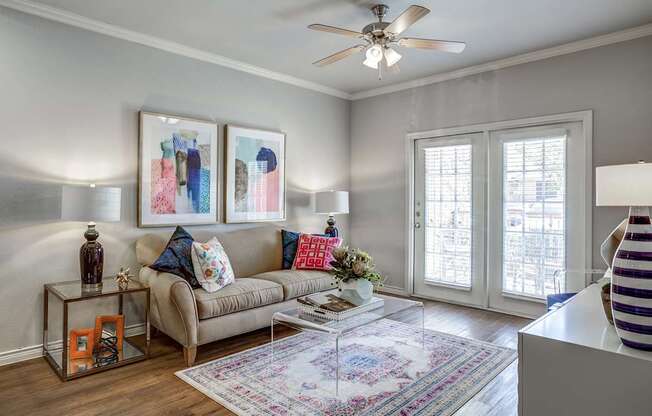 A living room with a beige couch, a glass table, and a ceiling fan.