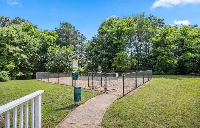 A green trash can sits on a concrete path next to a chain link fence.