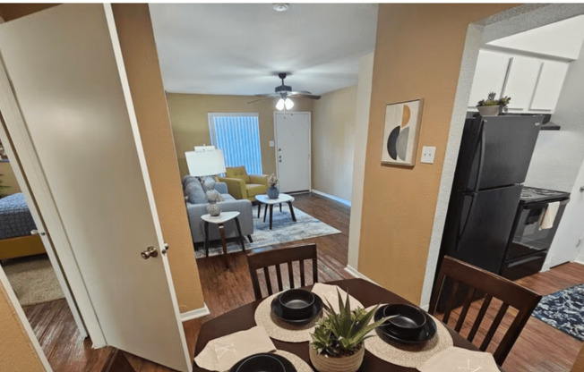 A dining room with a table set for two and a view of the living room.