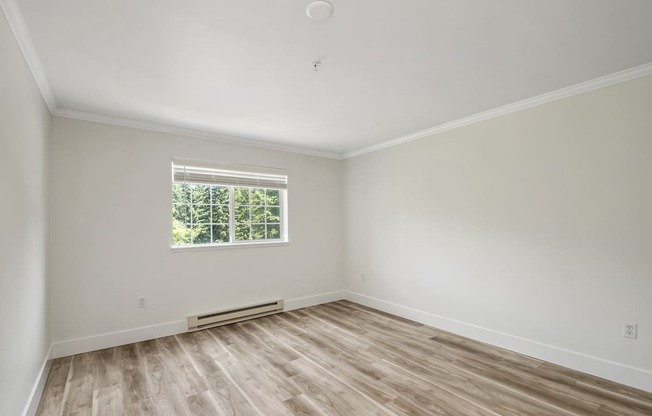 an empty bedroom with hardwood floors and a window