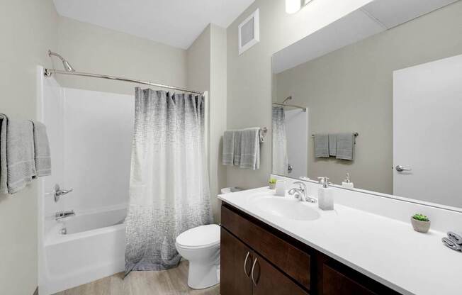 A bathroom with a white sink, toilet, and bathtub with grey shower curtain.