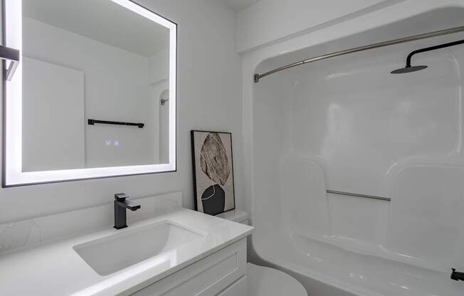 A white bathroom with a sink, mirror, and bathtub.