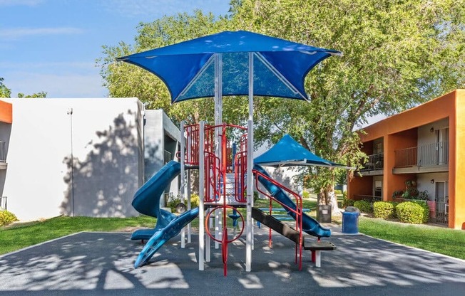 Community Playground with a Slide and Blue Canopy at Indigo Park Apartments in Albuquerque, NM.