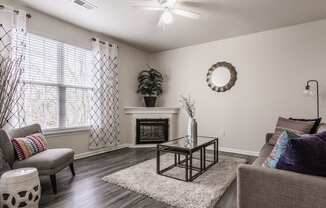 Eagle Creek, IN Apartments For Rent - Riverchase - Living Room With Hardwood Floors, A Ceiling Fan, A Decorative Fireplace, And A Window With Blinds