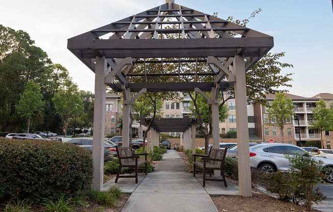 A wooden gazebo with a metal roof is situated in a parking lot.