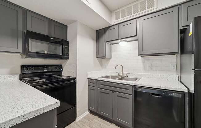 A kitchen with black appliances and grey cabinets.
