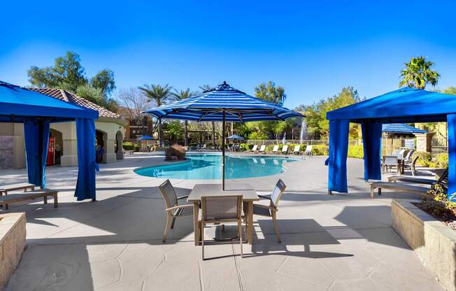 A pool area with a table and chairs under a blue canopy.