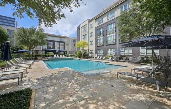 A swimming pool surrounded by lounge chairs and umbrellas in a courtyard.