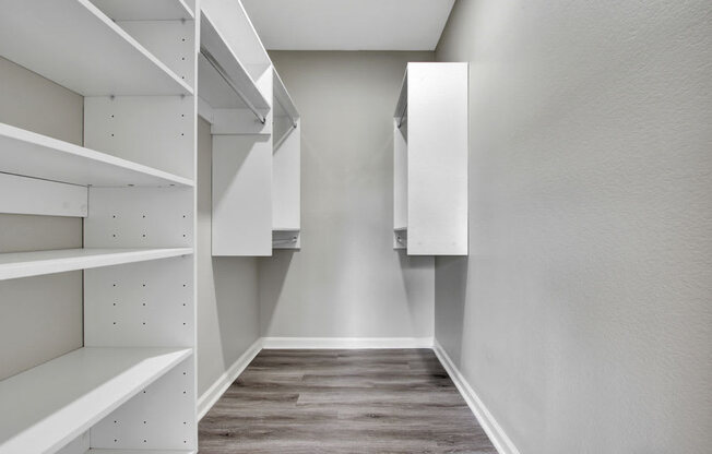 a walk in closet with white cabinets and a wooden floor