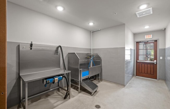 A clean, empty room with a stainless steel sink and a door with an exit sign above it.