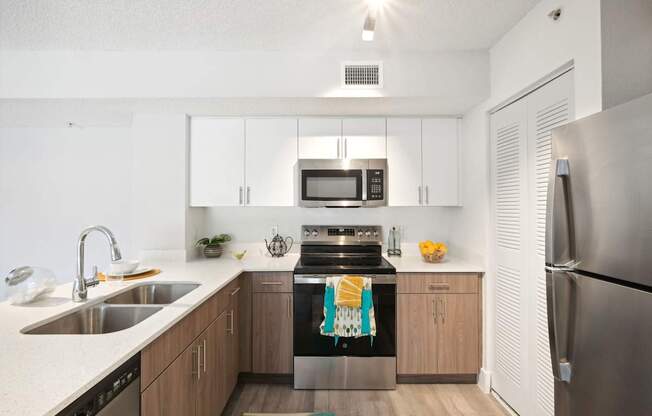 A modern kitchen with a stainless steel refrigerator, a stove with a towel on it, and a sink with a bowl on it.