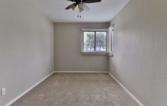 an empty bedroom with a window and a ceiling fan