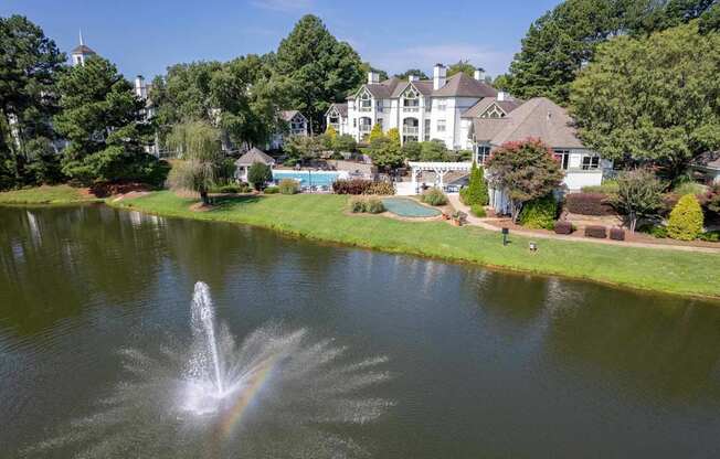 A fountain in the middle of a pond in front of a large house.