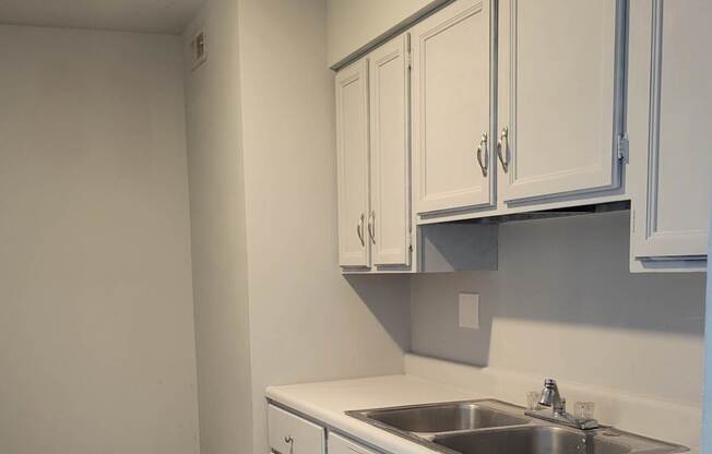 A kitchen with white cabinets and a white wall.