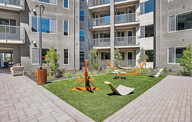 an apartment yard with hammocks and chairs in front of an apartment building