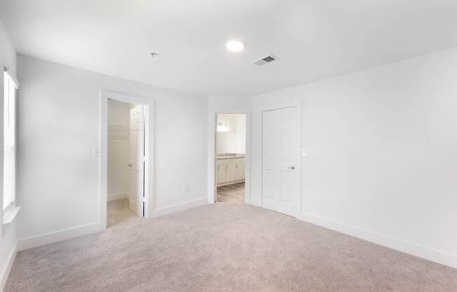 A spacious bed room with white walls and carpeted floor.