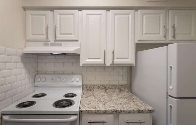 A kitchen with a white cabinets and a white appliances in a 2 bedroom, 1 bath apartment home at Harvard Square Apartments in the Vickery Midtown neighborhood of Dallas, TX.