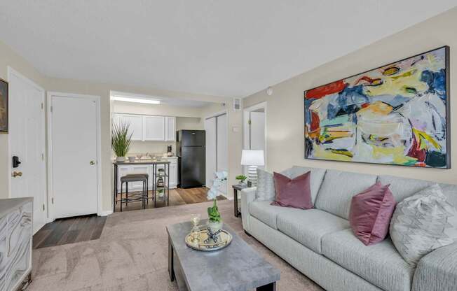 A living room with a grey couch and a painting on the wall.