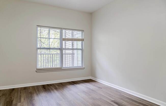 a bedroom with white walls and a window and wood floors