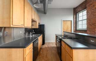 a kitchen with wooden cabinets and black counter tops and a brick wall