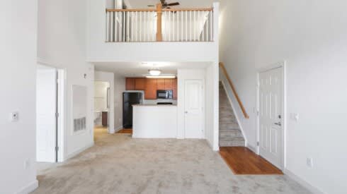an empty living room with a kitchen and a staircase