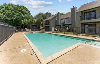 A swimming pool surrounded by a fence and a building in the background.