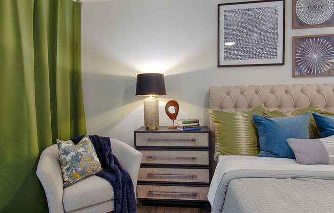 A bedroom with a bed, chair, and nightstand.