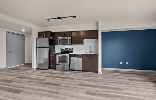 an empty room with a blue wall and a kitchen with stainless steel appliances