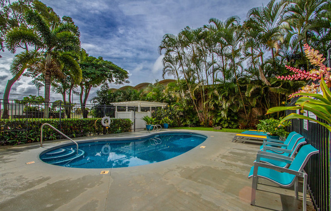 a swimming pool and chairs in a backyard with palm trees at Palms of Kilani Apartments, Wahiawa, HI 96786