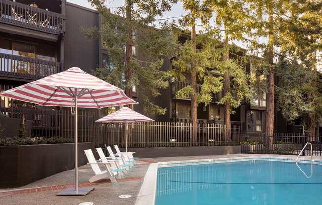 a pool with chairs and an umbrella in front of a building