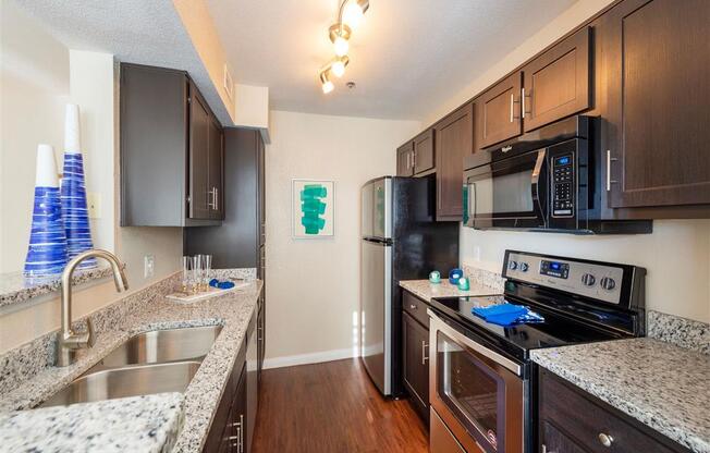 Two BR Apartments in League City, TX - Anchor at South Shore - Kitchen with Granite Countertops, Dark Wood Cabinetry, Stainless Steel Appliances, Wood-Style Flooring, and Ceiling Light Fixtures