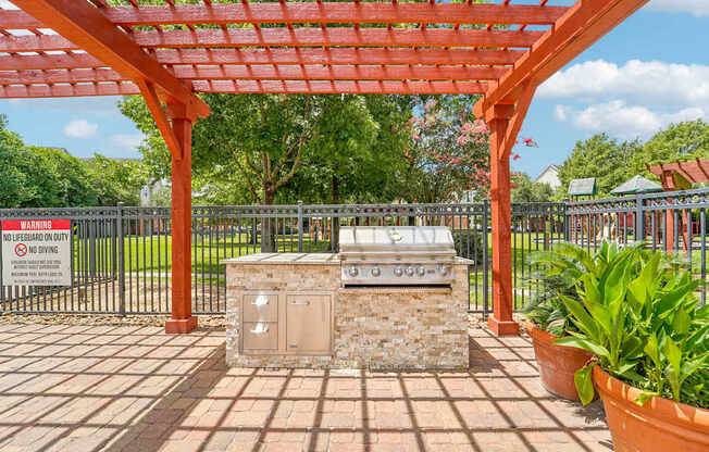 A red pergola is over a stone structure in a park.