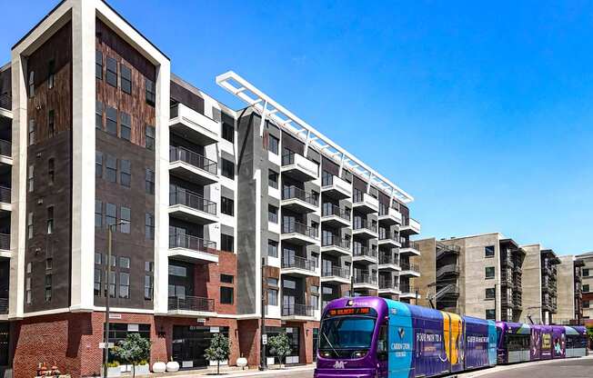 A purple train is on the tracks in front of a building.