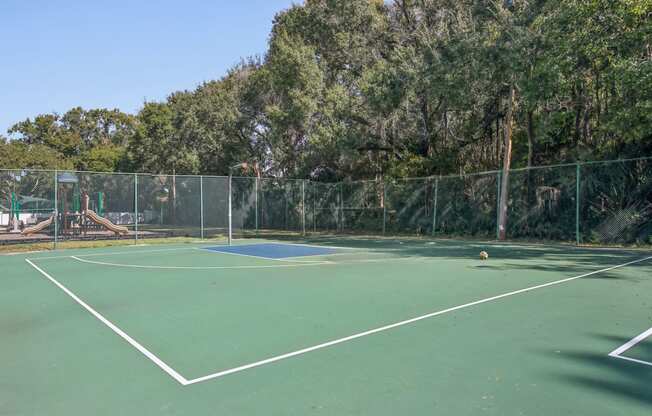 A tennis court surrounded by a fence and trees.