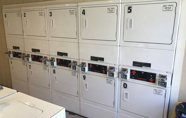 A row of white washing machines with numbered doors.