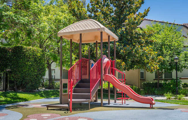 A playground with a red slide and a brown roofed pavilion.