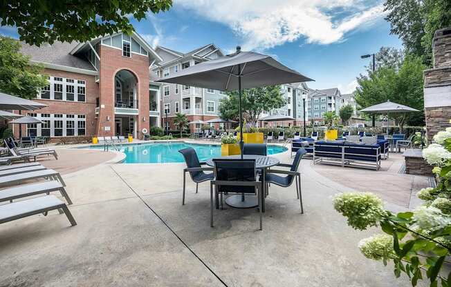A pool area with chairs and umbrellas in front of a building.