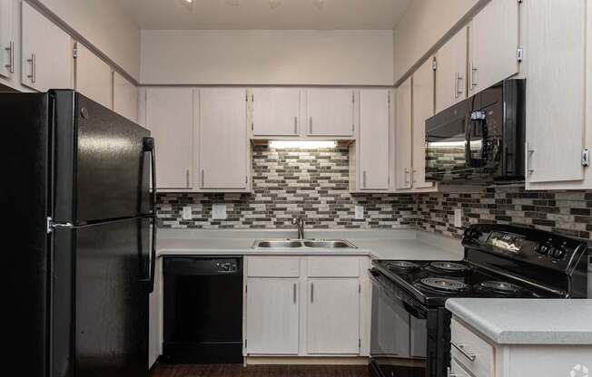 A black refrigerator is on the left in a kitchen with white cabinets.