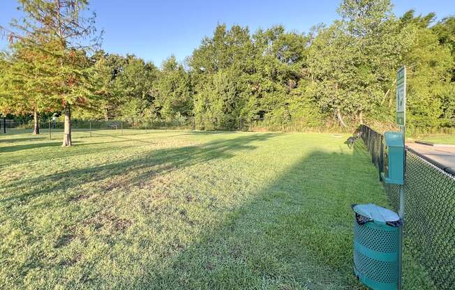 a grassy field with a fence and a trash can