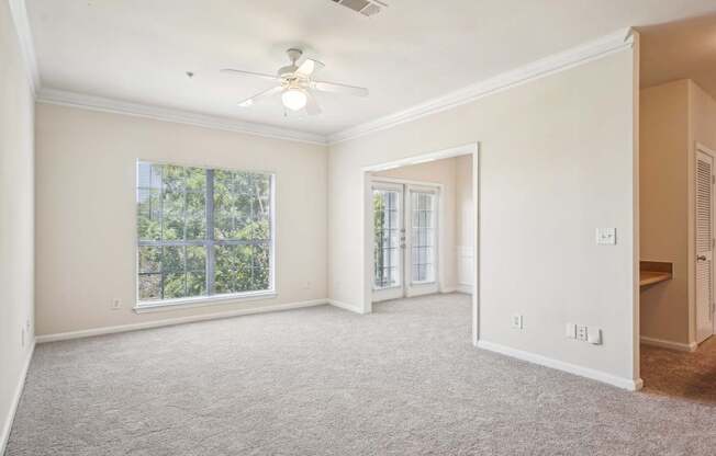 A spacious living room with a ceiling fan, carpeted floor and windows.
