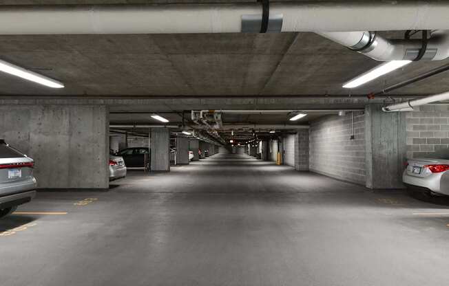A long, narrow parking garage with concrete walls and ceiling, and cars parked on both sides.