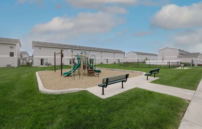 A playground with a green slide and two benches.