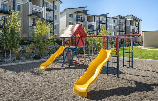 a playground with slides and a swing set in front of an apartment building